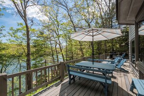 Eine Holzterrasse mit blauen Bänken und einem Tisch, mit Blick auf einen von Bäumen umgebenen See.