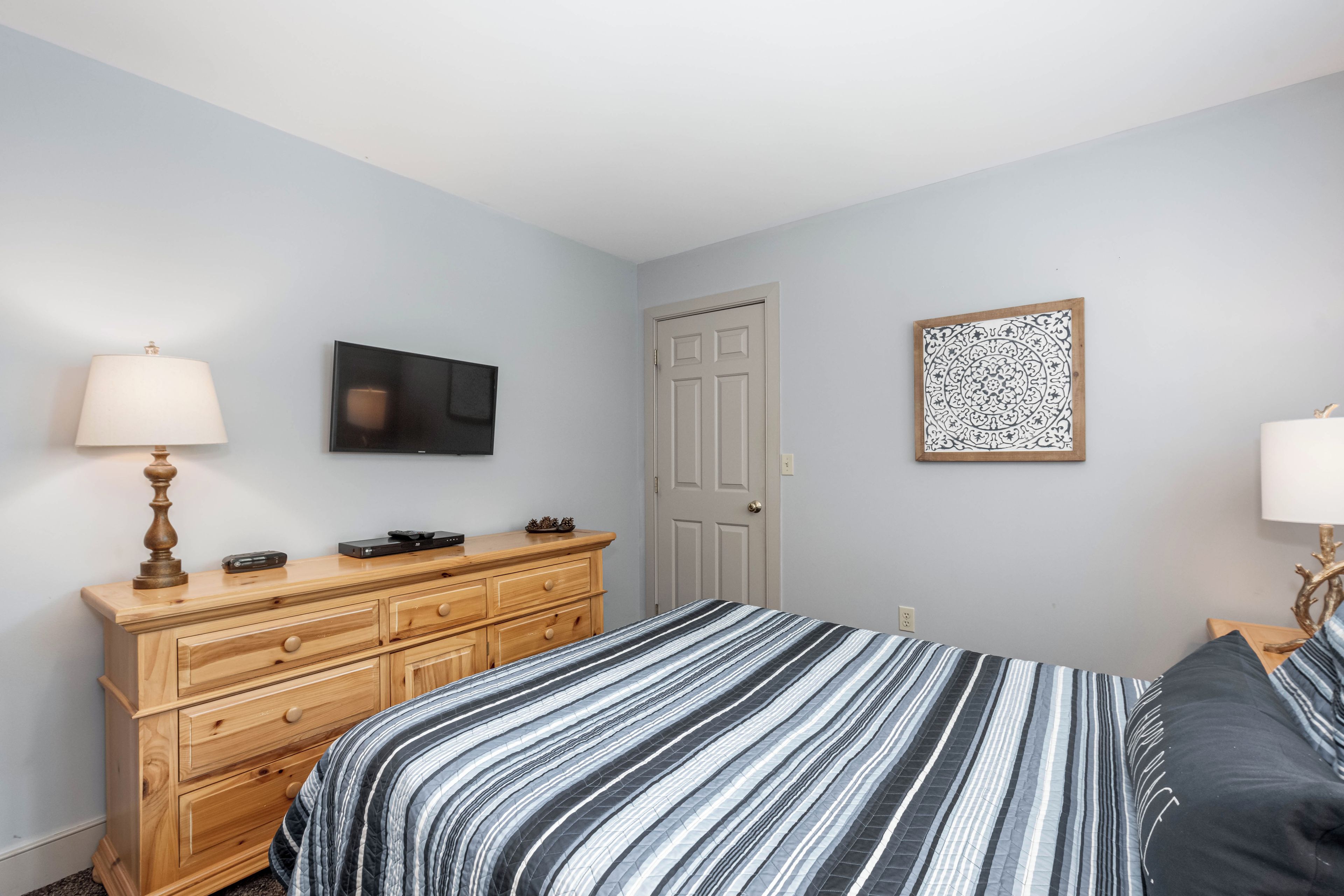 Een slaapkamer met een bed, een dressoir, een televisie, een deur en kunst aan de muur.