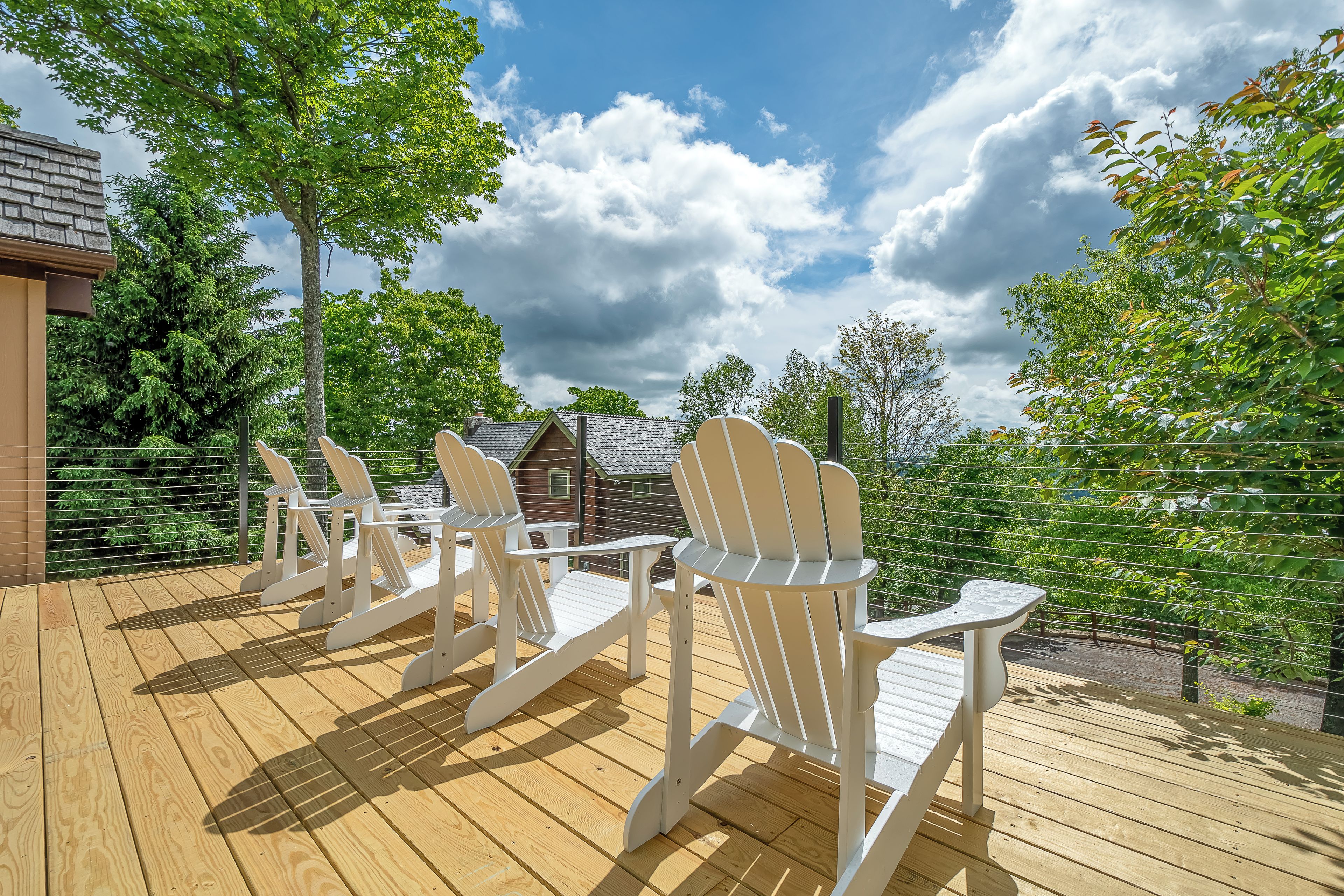 A wooden deck with Adirondack chairs and a view of a house and trees.