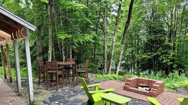 An outdoor patio with a brick fire pit, green and brown wooden furniture, and a covered seating area.