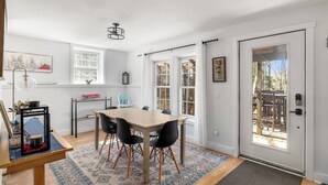 A dining area with a table and chairs, a rug, and a door leading outside.
