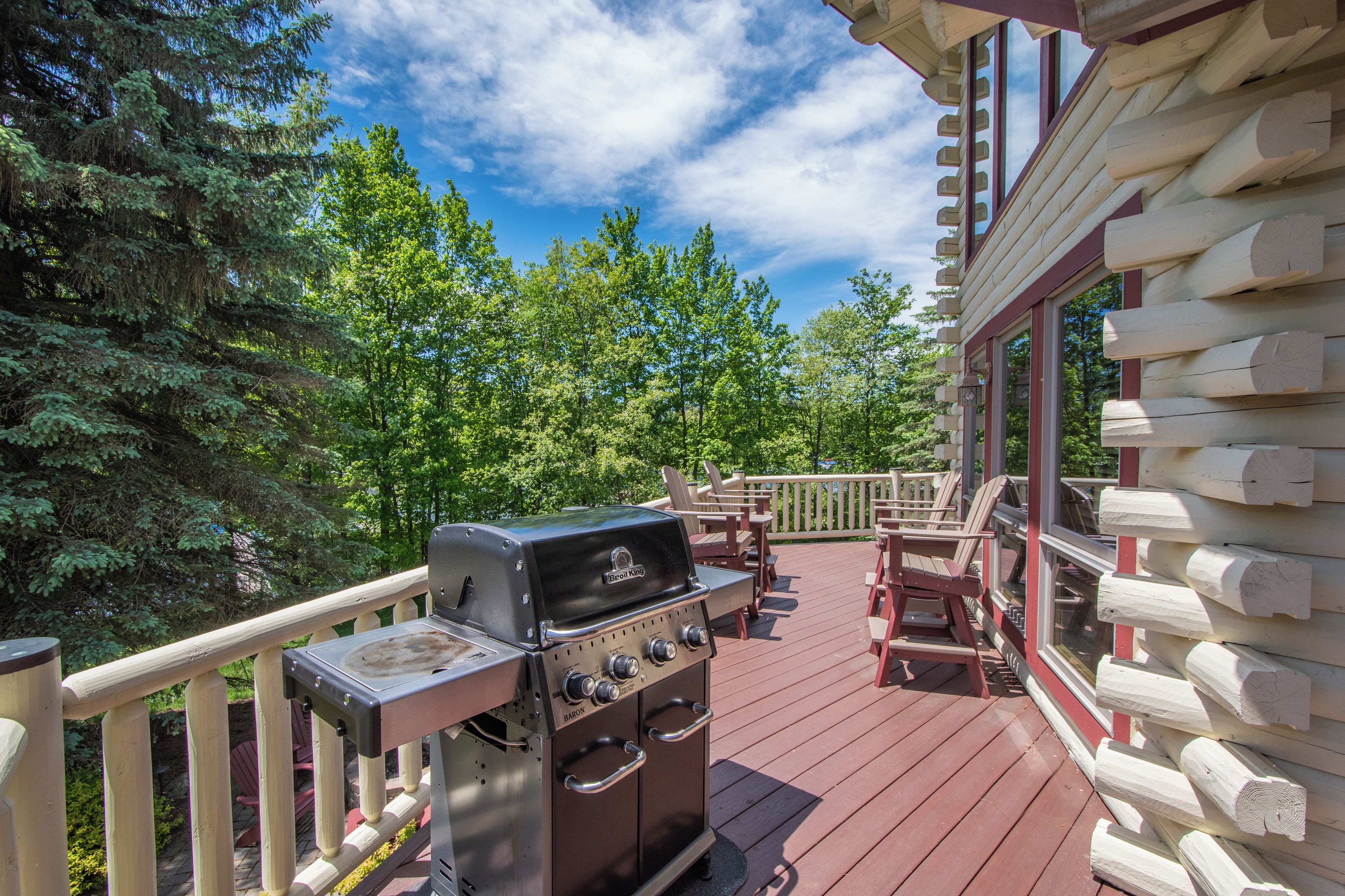 A wooden deck with a grill, outdoor furniture, and a view of trees.