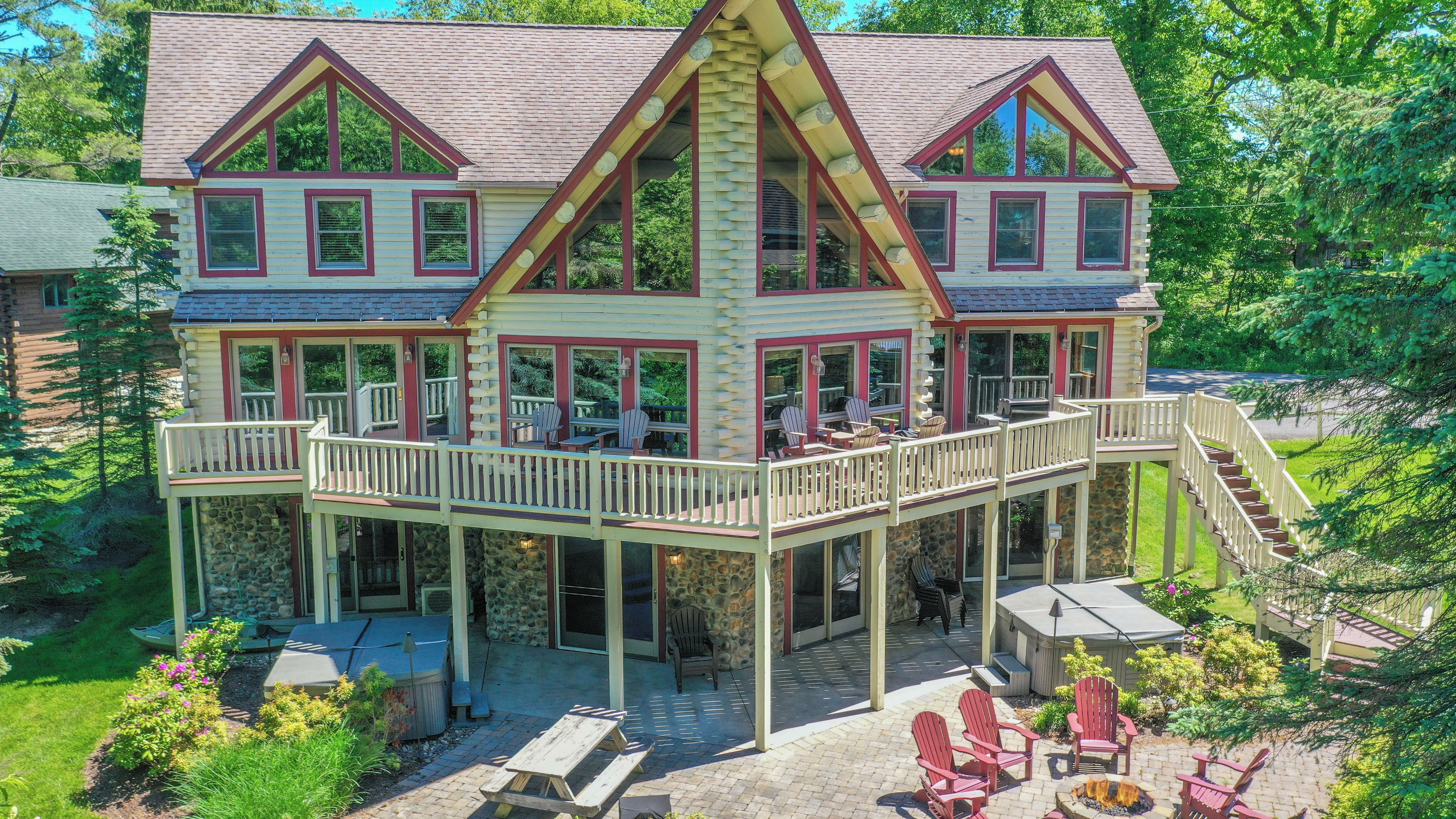 A large, multi-story log cabin with a wrap-around deck, outdoor seating, and a fire pit.