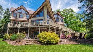 A large, multi-story house with a prominent balcony and a stone foundation. - Mallard Landing by Taylor Made Deep Creek (McHenry)