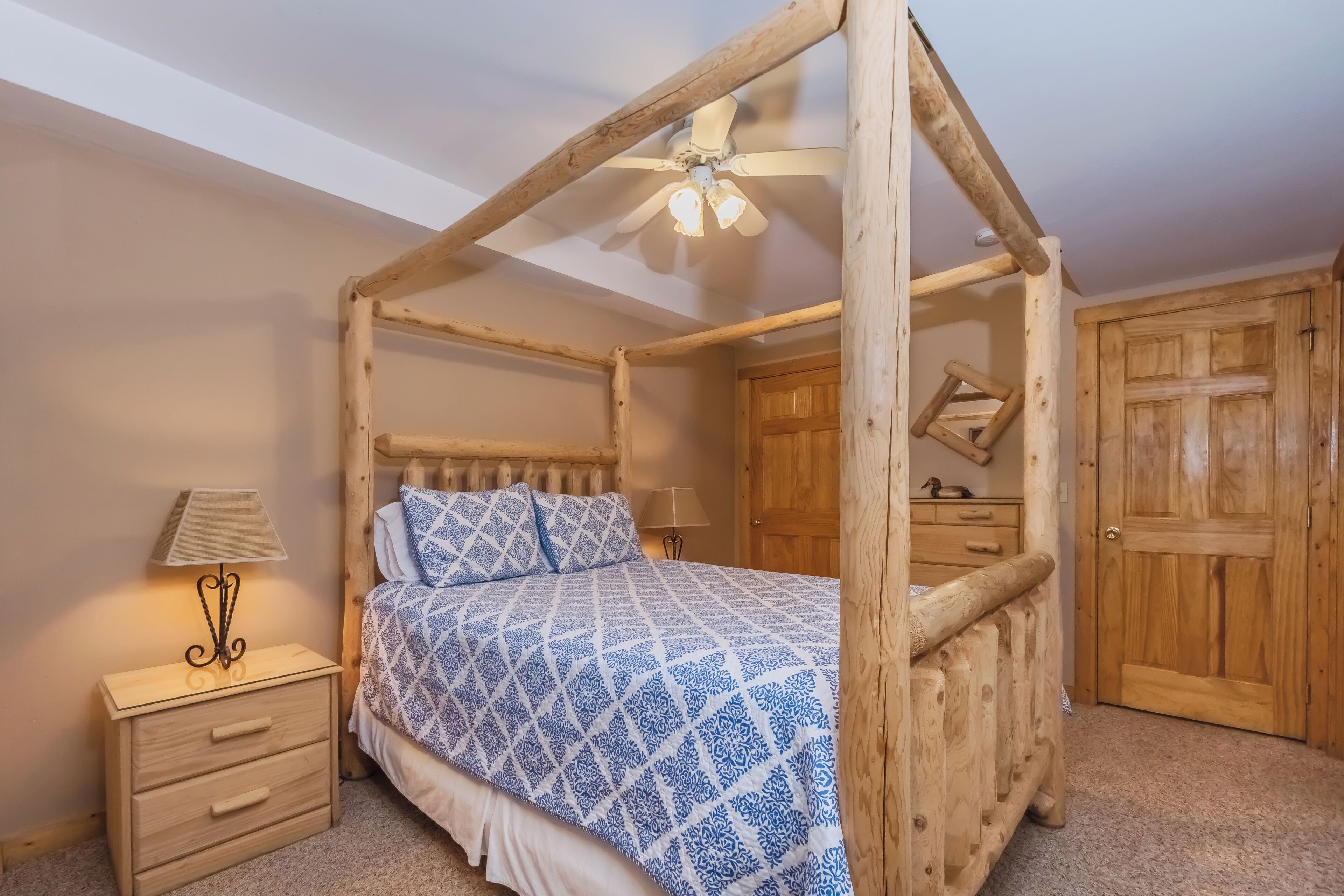 Una cama con dosel de madera, con un edredón estampado, una mesita de noche con lámpara y armarios de madera.