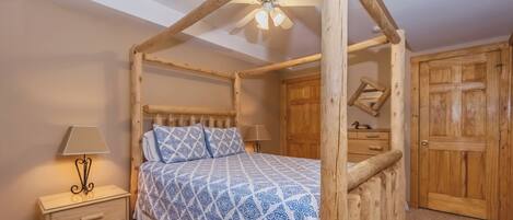 Una cama con dosel de madera, con un edredón estampado, una mesita de noche con lámpara y armarios de madera.