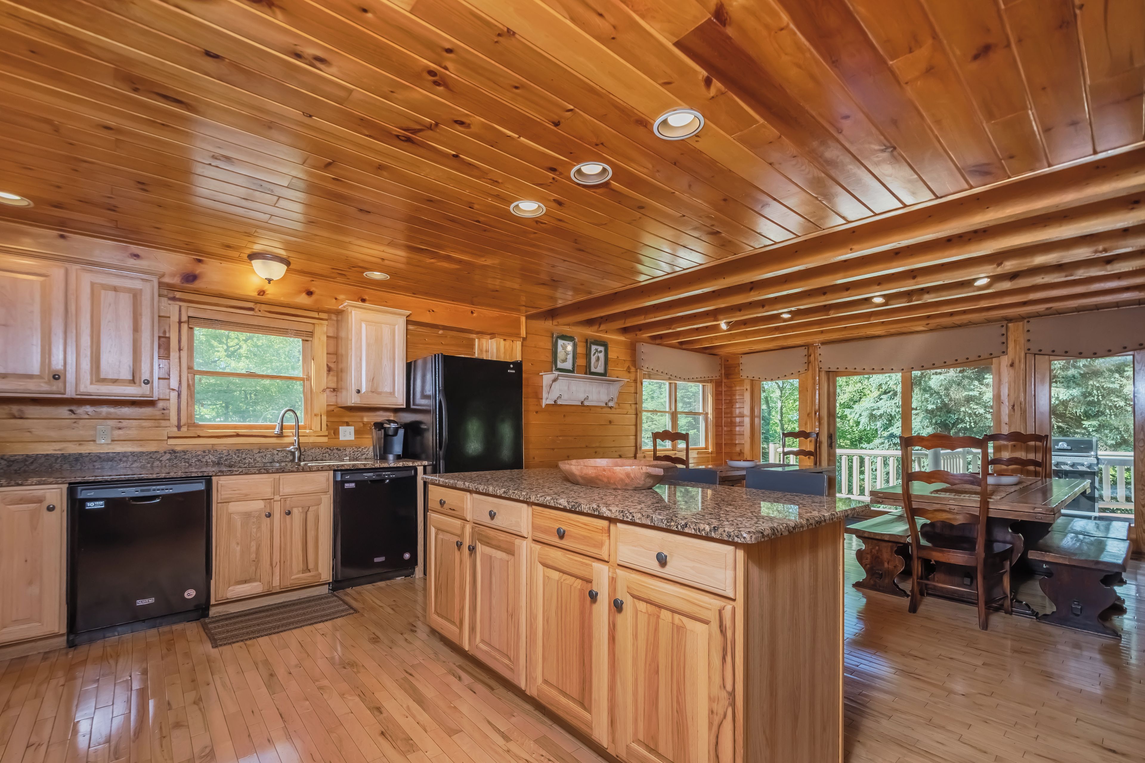 L’intérieur d’un chalet en bois comprend une cuisine équipée de meubles en bois, de plans de travail en granit et d’un coin repas avec une table et des chaises.