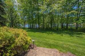 A grassy area with a stone pathway leading to a body of water, surrounded by trees.