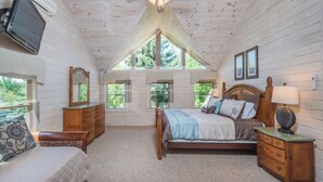 A bedroom with a wooden ceiling, a bed with a headboard, a nightstand, a dresser, and a TV mounted on the wall. - Mallard Landing by Taylor Made Deep Creek (McHenry)