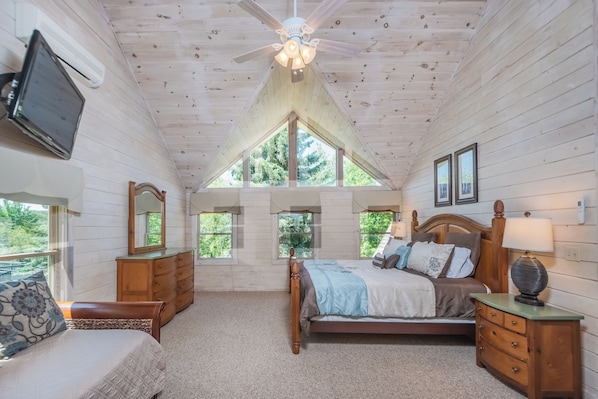 A bedroom with a wooden ceiling, a bed with a headboard, a nightstand, a dresser, and a TV mounted on the wall.