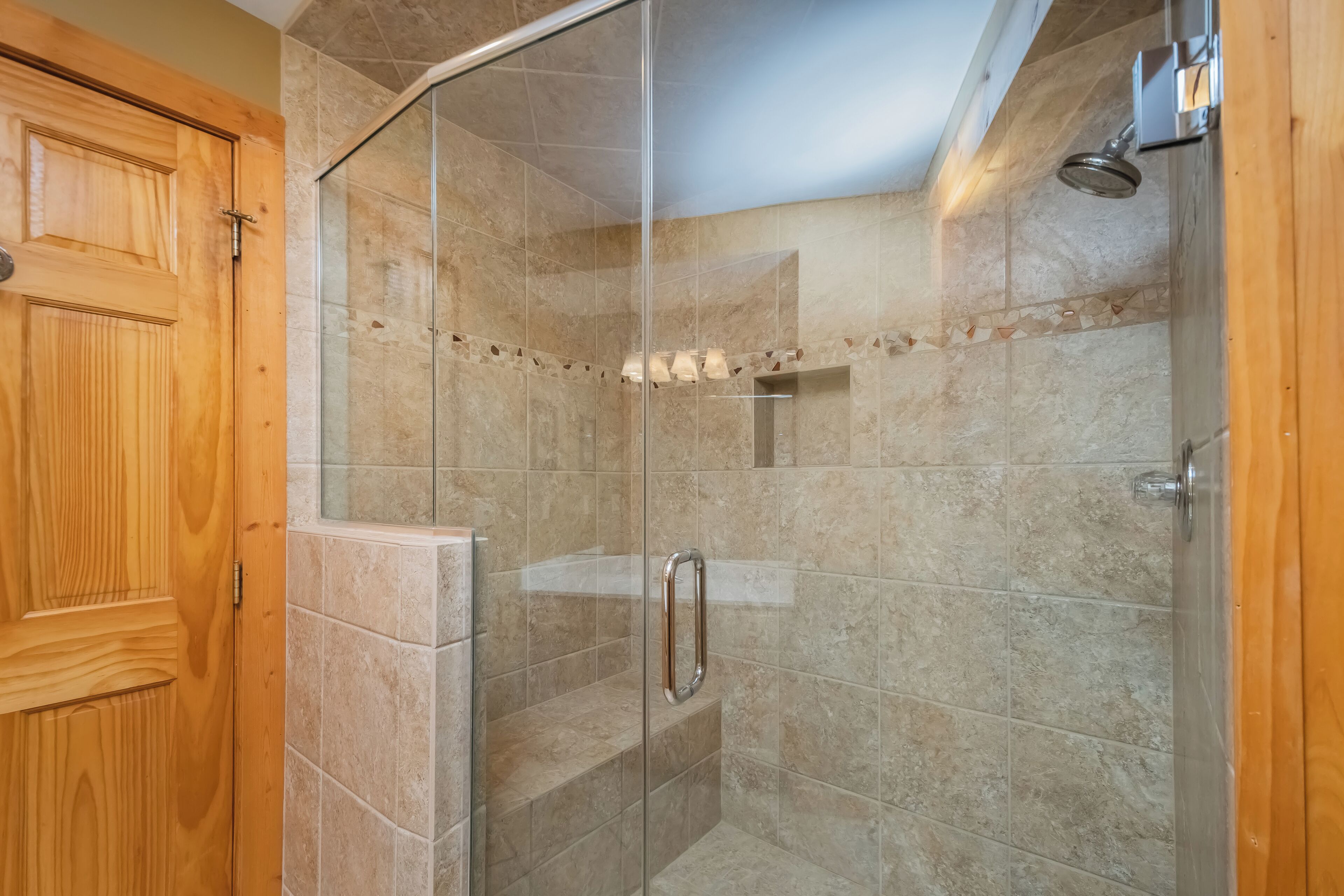A glass-enclosed shower with beige tiles and a wooden door.