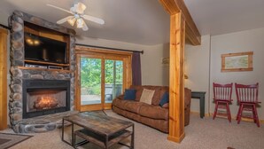 A cozy living room with a stone fireplace, a brown leather couch, and a wooden coffee table. - Mallard Landing by Taylor Made Deep Creek (McHenry)
