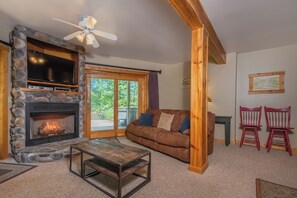 A cozy living room with a stone fireplace, a brown leather couch, and a wooden coffee table. - Mallard Landing by Taylor Made Deep Creek (McHenry)