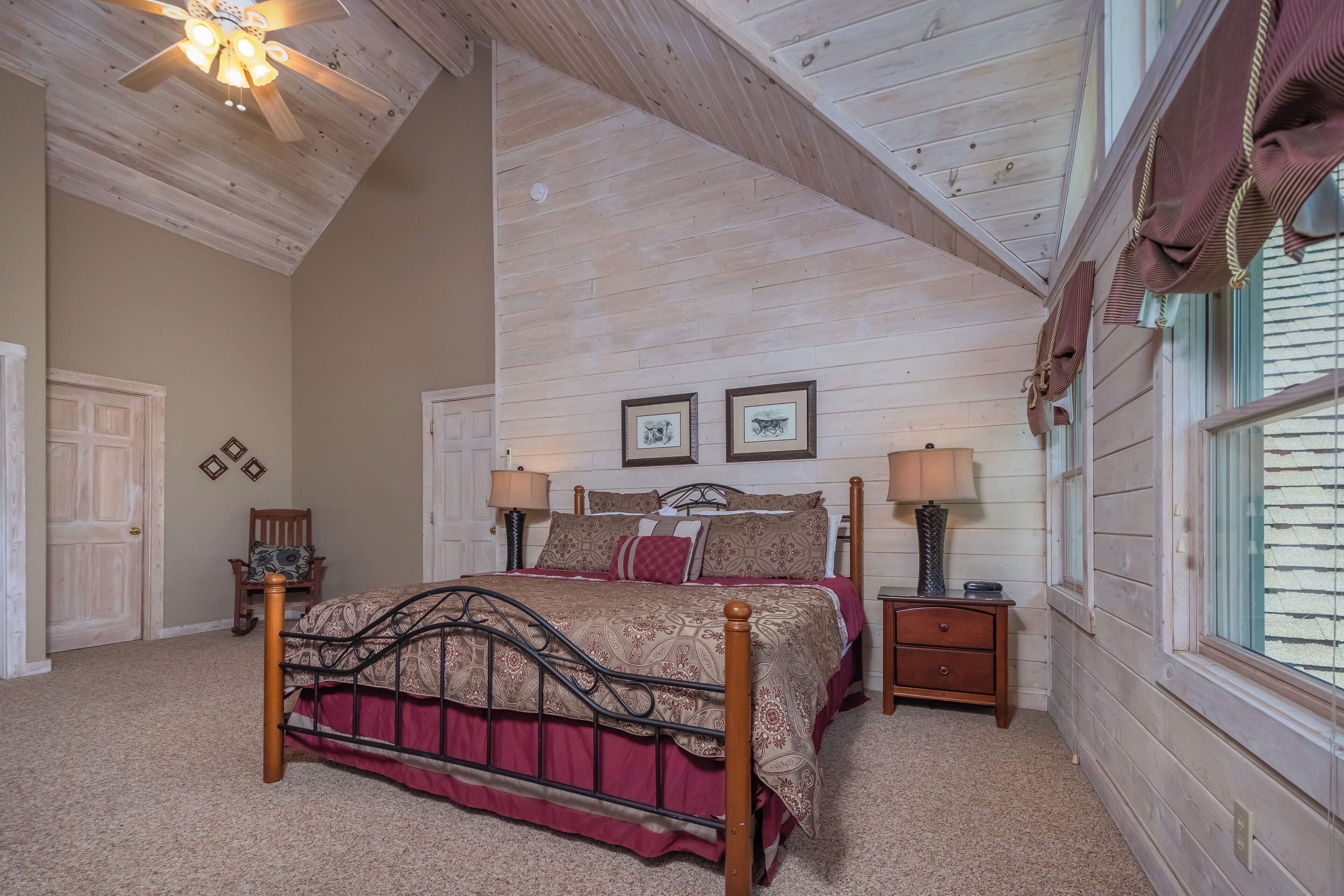 A bedroom with a wooden ceiling, a bed with a metal frame, two bedside tables with lamps, and a window with curtains.