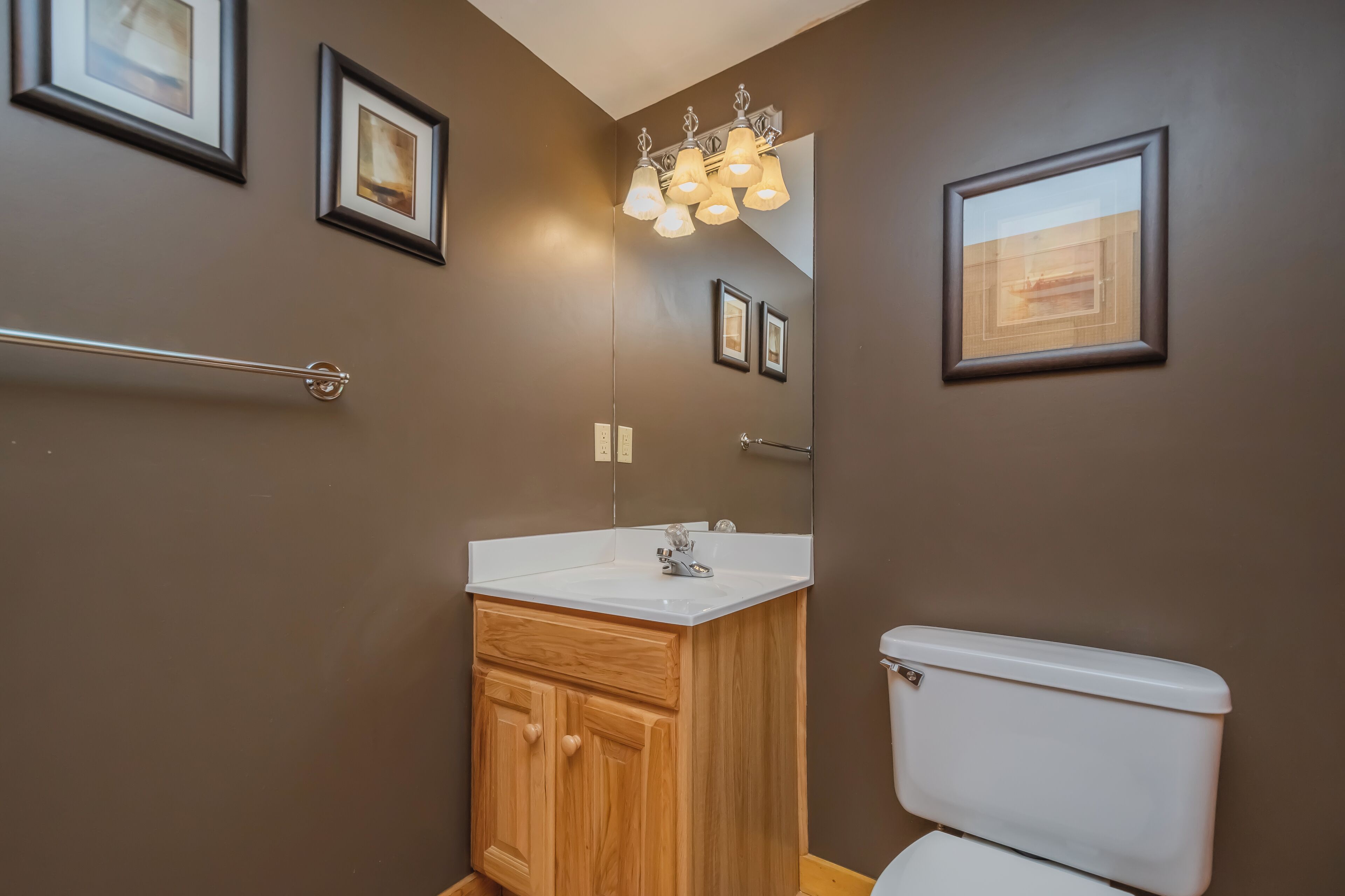 A modern bathroom with a wooden vanity, a white toilet, and framed pictures on the walls.