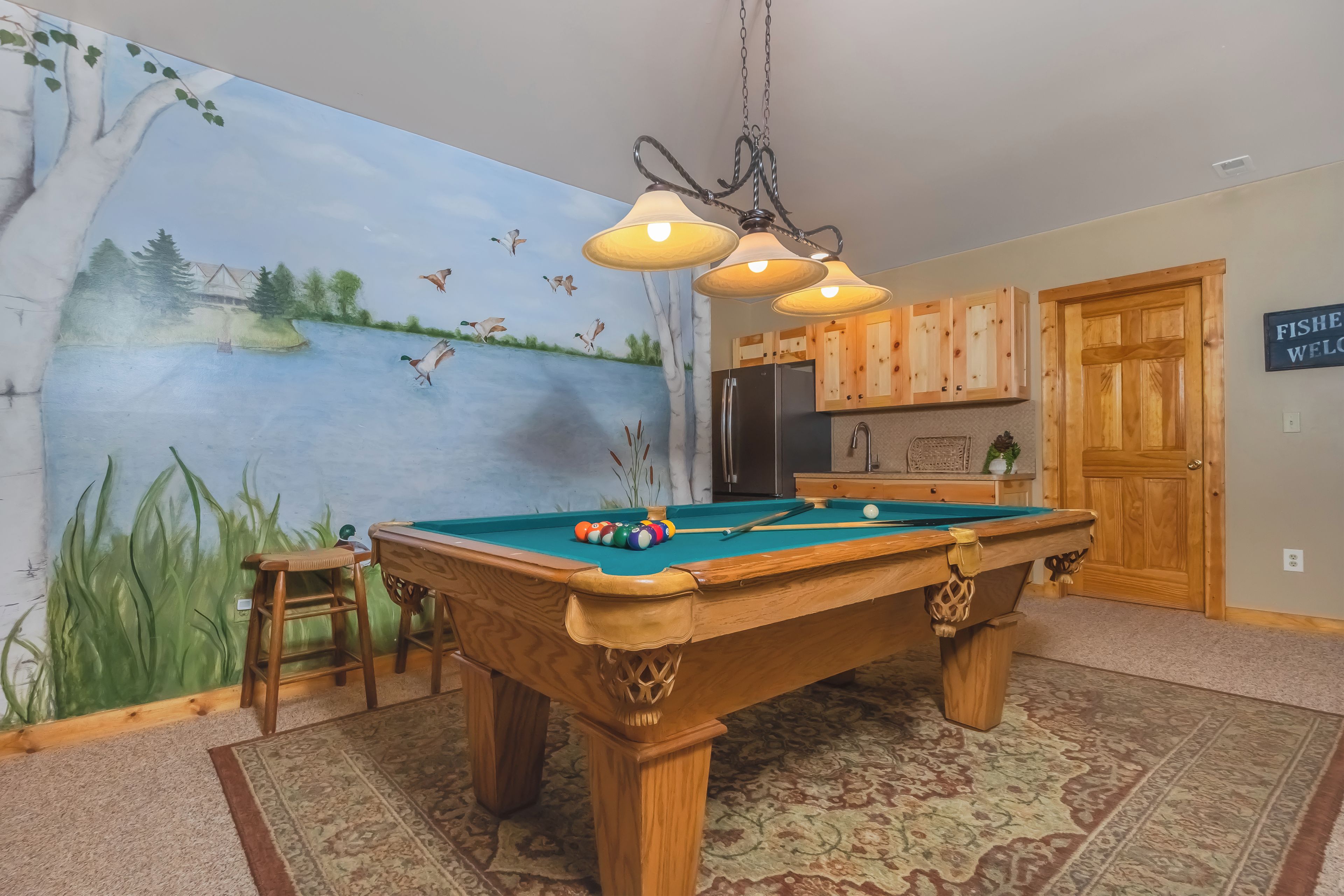 Une table de billard ornée d’une fresque représentant un lac et des oiseaux sur le mur, des meubles en bois et un panneau d’accueil.