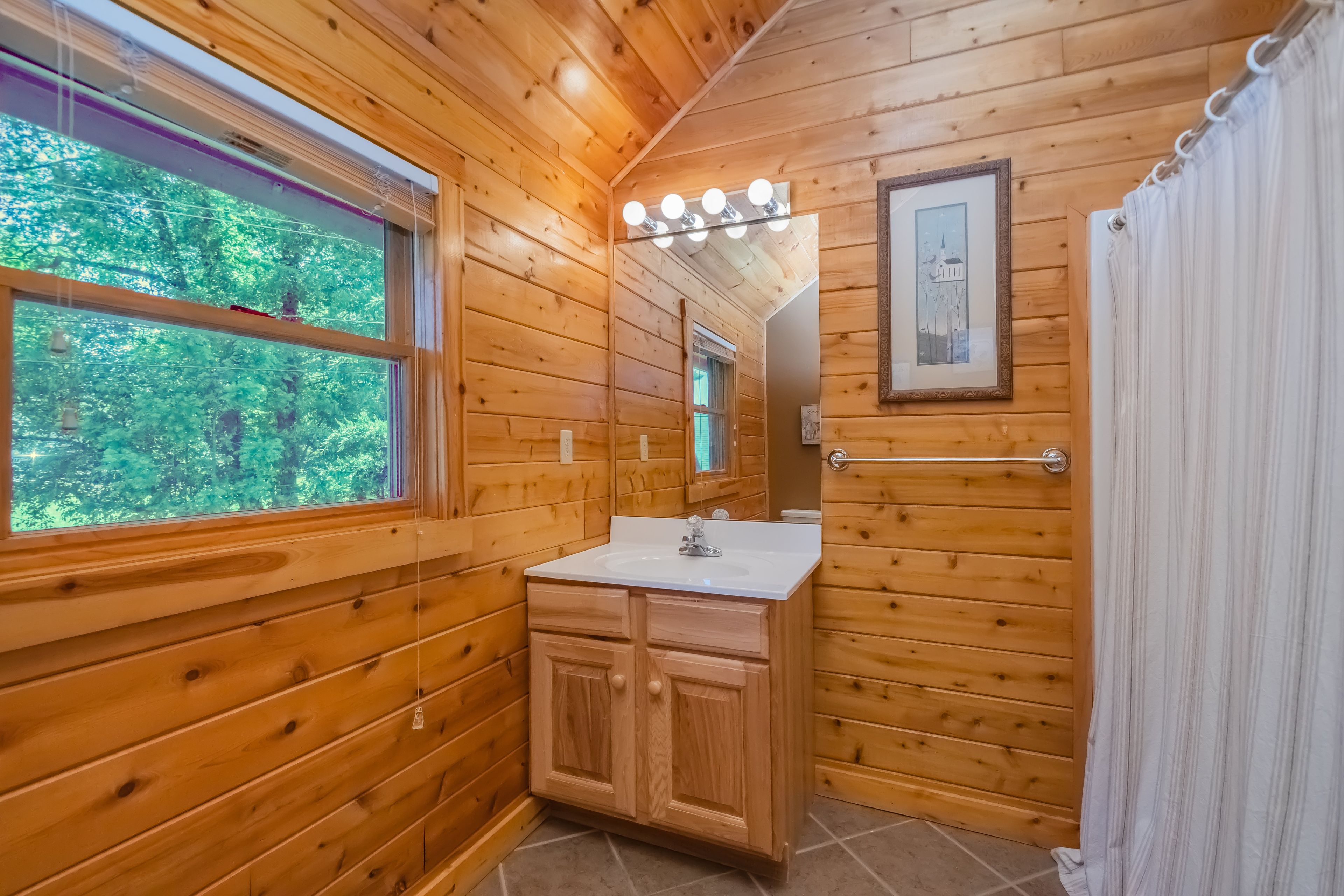 A wooden cabin bathroom with a sink, mirror, and window.