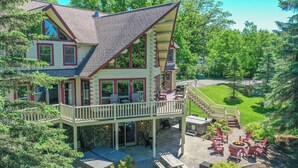 A two-story log cabin with a balcony and outdoor seating area. - Mallard Landing by Taylor Made Deep Creek (McHenry)