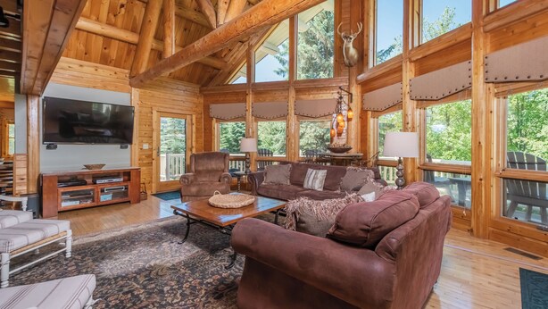 A spacious living room with a large brown leather sofa, a wooden coffee table, and a flat-screen TV mounted on the wall. - Mallard Landing by Taylor Made Deep Creek (McHenry)