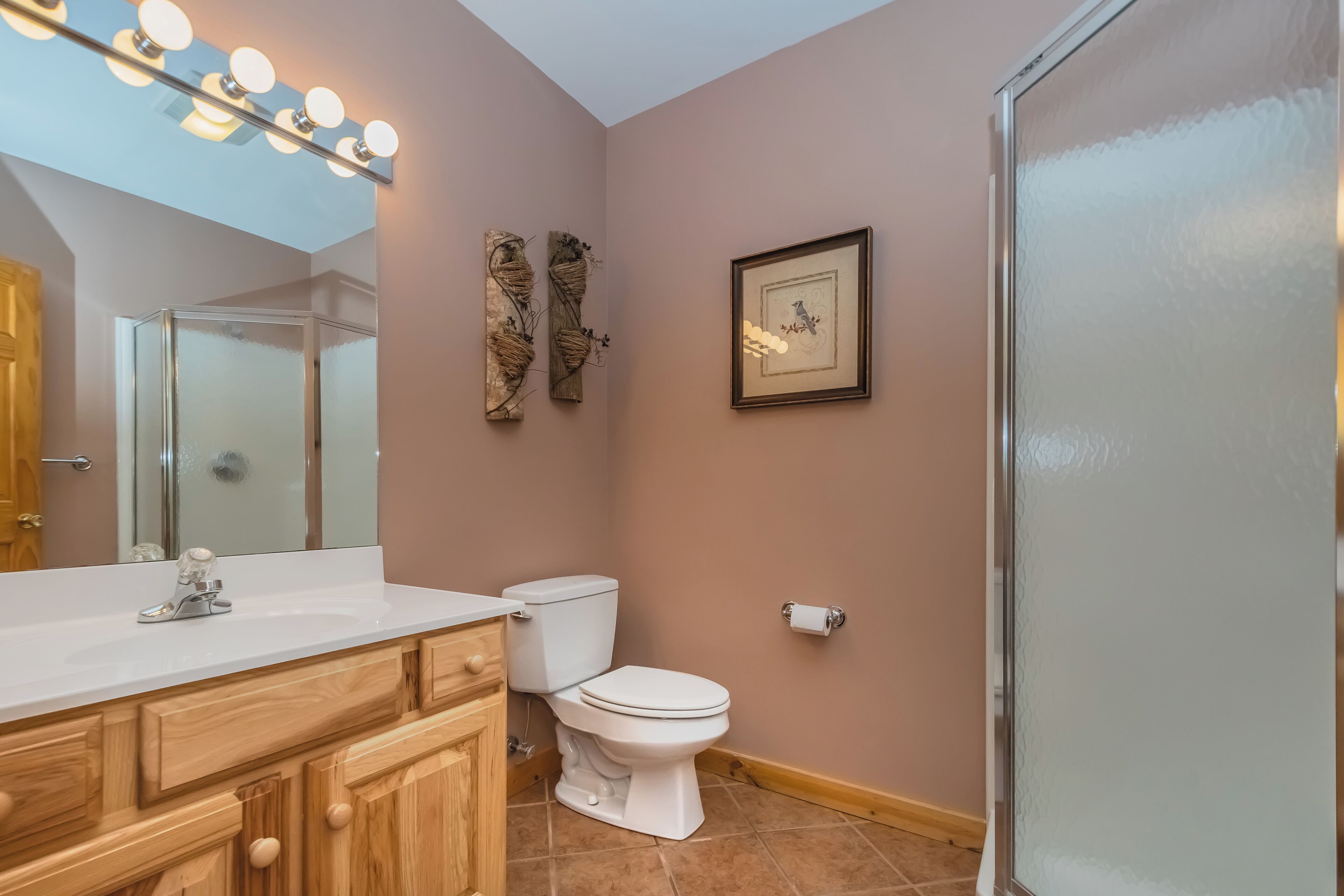 Une salle de bain comprenant un meuble-lavabo, des toilettes, un miroir avec éclairage intégré et des éléments de décoration fixés au mur.