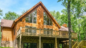 Une cabane en rondins dotée d’un balcon, de fondations en pierre et d’une terrasse en bois.