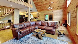 L’intérieur d’un chalet en bois, avec un canapé d’angle en cuir, une table à manger et un escalier.