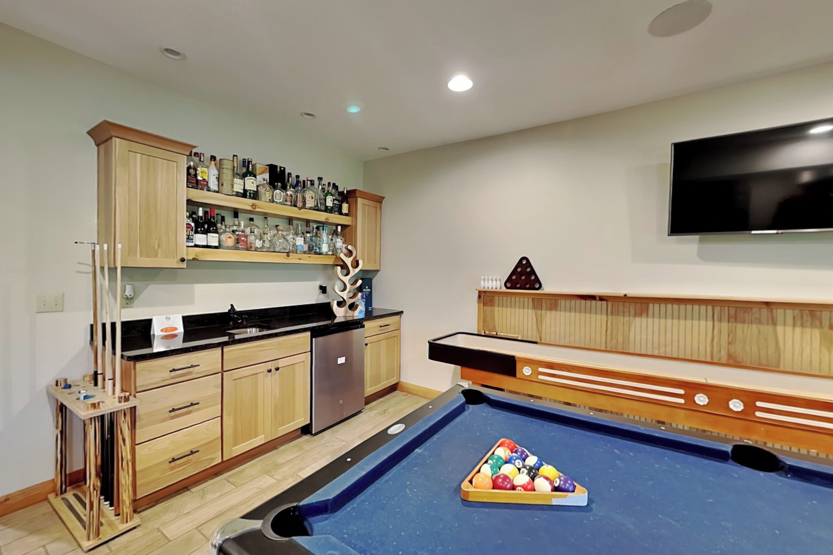Een pooltafel met een breek, een bar met drankflessen en een flatscreen tv aan de muur.