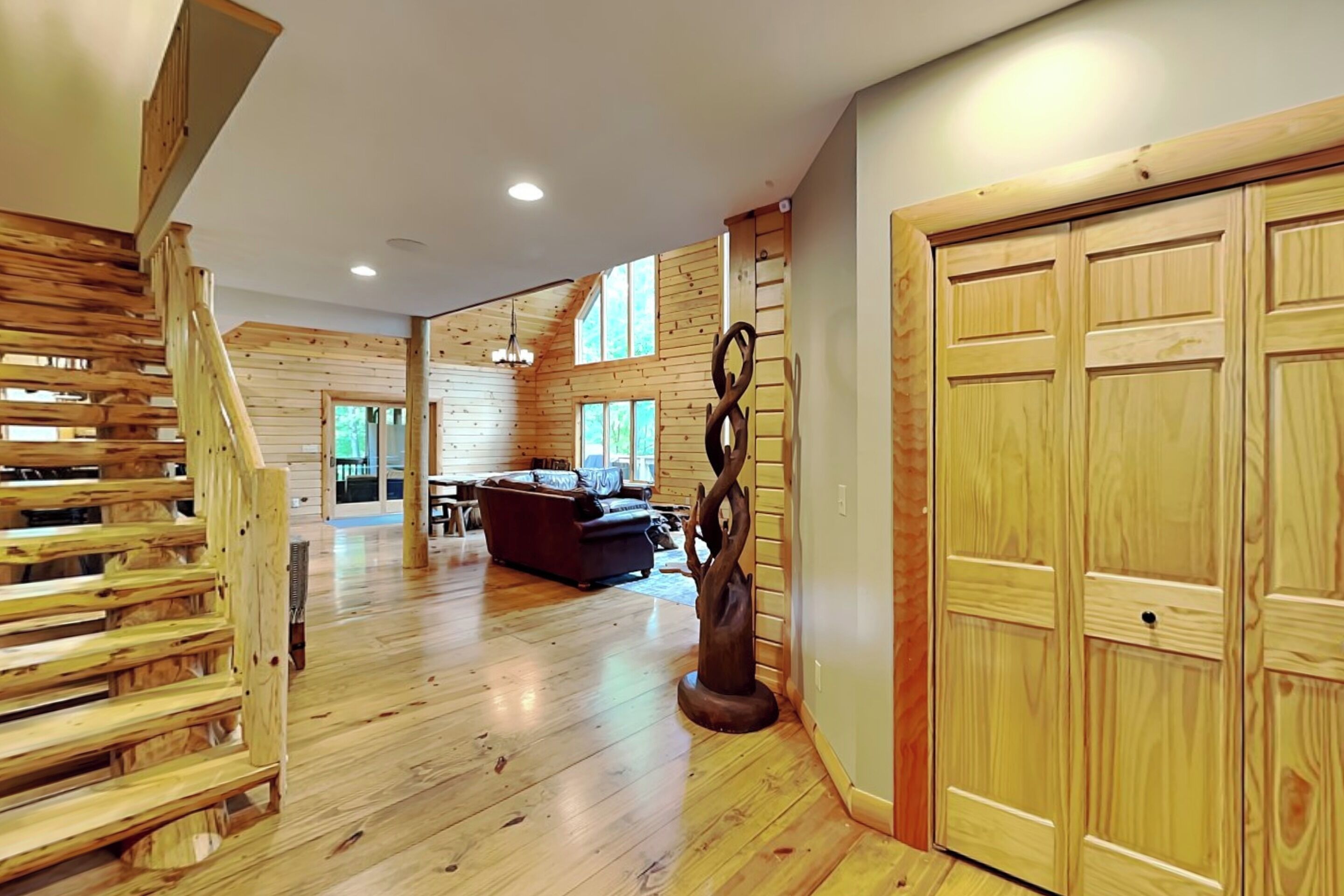 A spacious room with wooden floors, a staircase, a dining area, and a large wooden door.