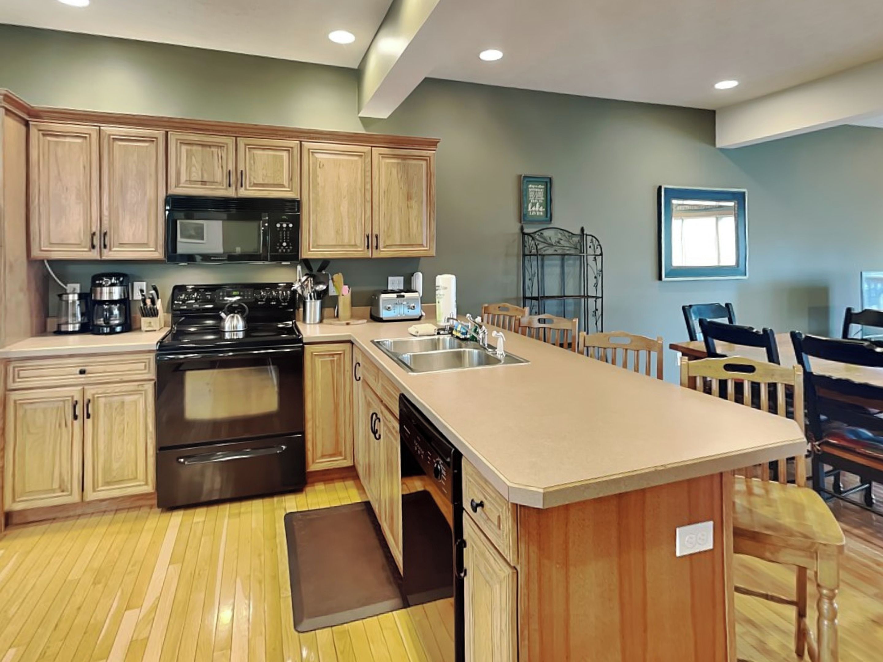 A kitchen with wooden cabinets, a black stove, a microwave, and a sink. There is a dining area with wooden chairs and a table.