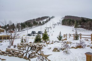 A snow-covered ski slope with a ski lift, wooden fence, and sparse trees.