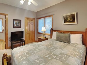 A bedroom with a bed, a television, a nightstand, a lamp, and a window with blinds. - Marsh Run Cove by Taylor Made Deep Creek (McHenry)
