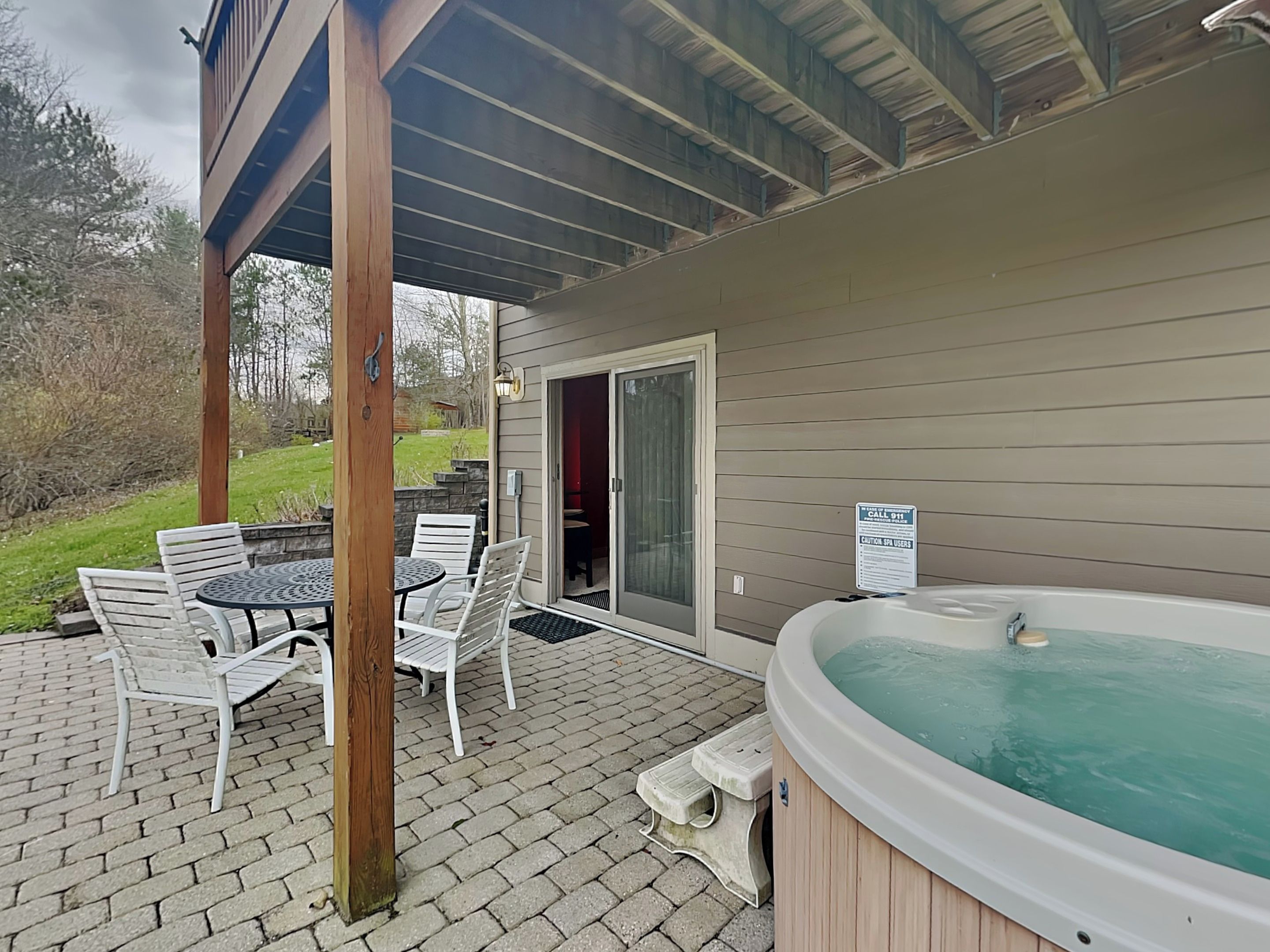 An outdoor patio with a hot tub, a table with chairs, and a covered area with a wooden ceiling.