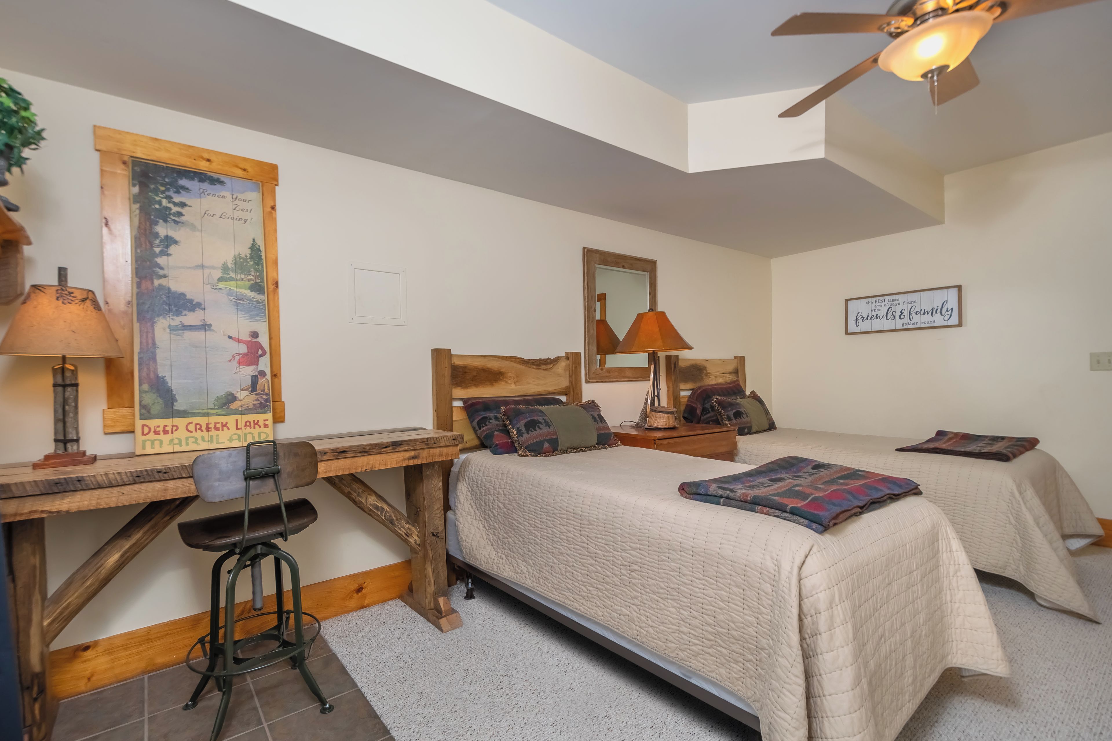 A bedroom with two beds, a desk, and a chair. There is a ceiling fan and a poster on the wall.