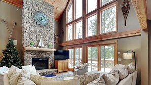 A cozy living room with a stone fireplace, a large window, and a Christmas tree. - Midnight Dip by Taylor Made Deep Creek (Swanton)