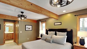 A bedroom with a large bed, wooden ceiling beams, a nightstand with a lamp, and a framed picture on the wall. - Midnight Dip by Taylor Made Deep Creek (Swanton)