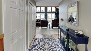 A hallway with a patterned rug, a console table with decorative items, and a large mirror on the wall. - Million Dollar View by Taylor Made Deep Creek (McHenry)