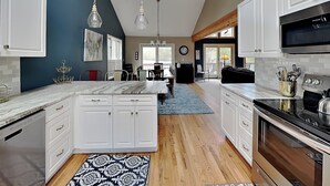 A modern kitchen with white cabinets, a central island, and a dining area with chairs. - Million Dollar View by Taylor Made Deep Creek (McHenry)