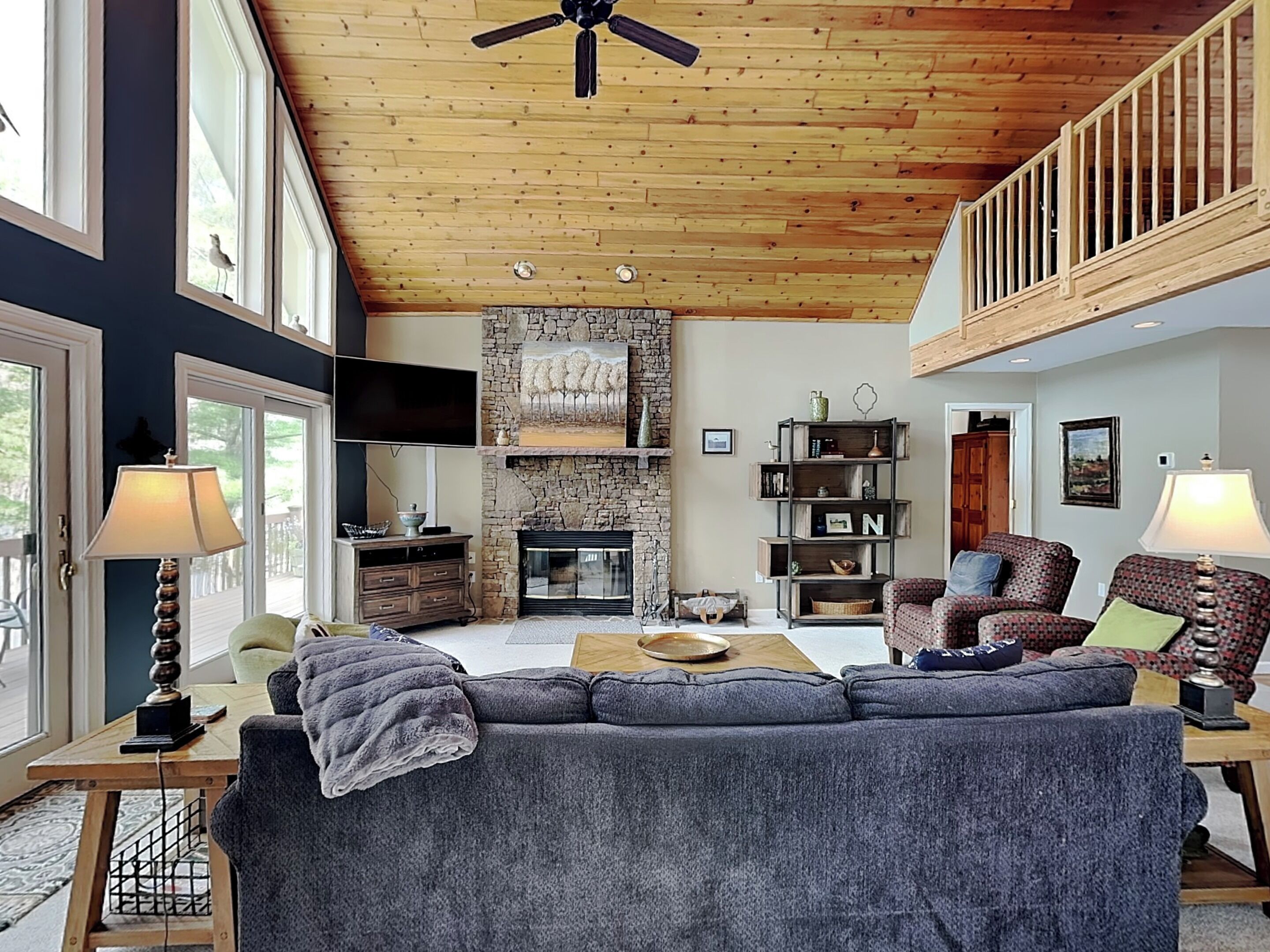 Un salón amplio con chimenea de piedra, techo de madera y balcón.