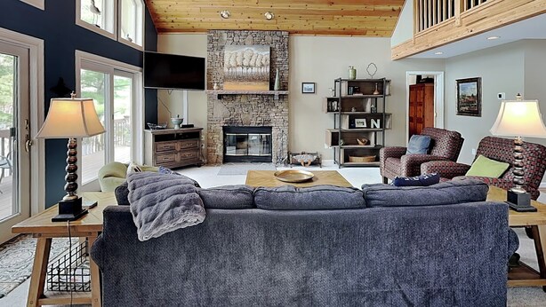 A spacious living room with a stone fireplace, wooden ceiling, and a balcony. - Million Dollar View by Taylor Made Deep Creek (McHenry)