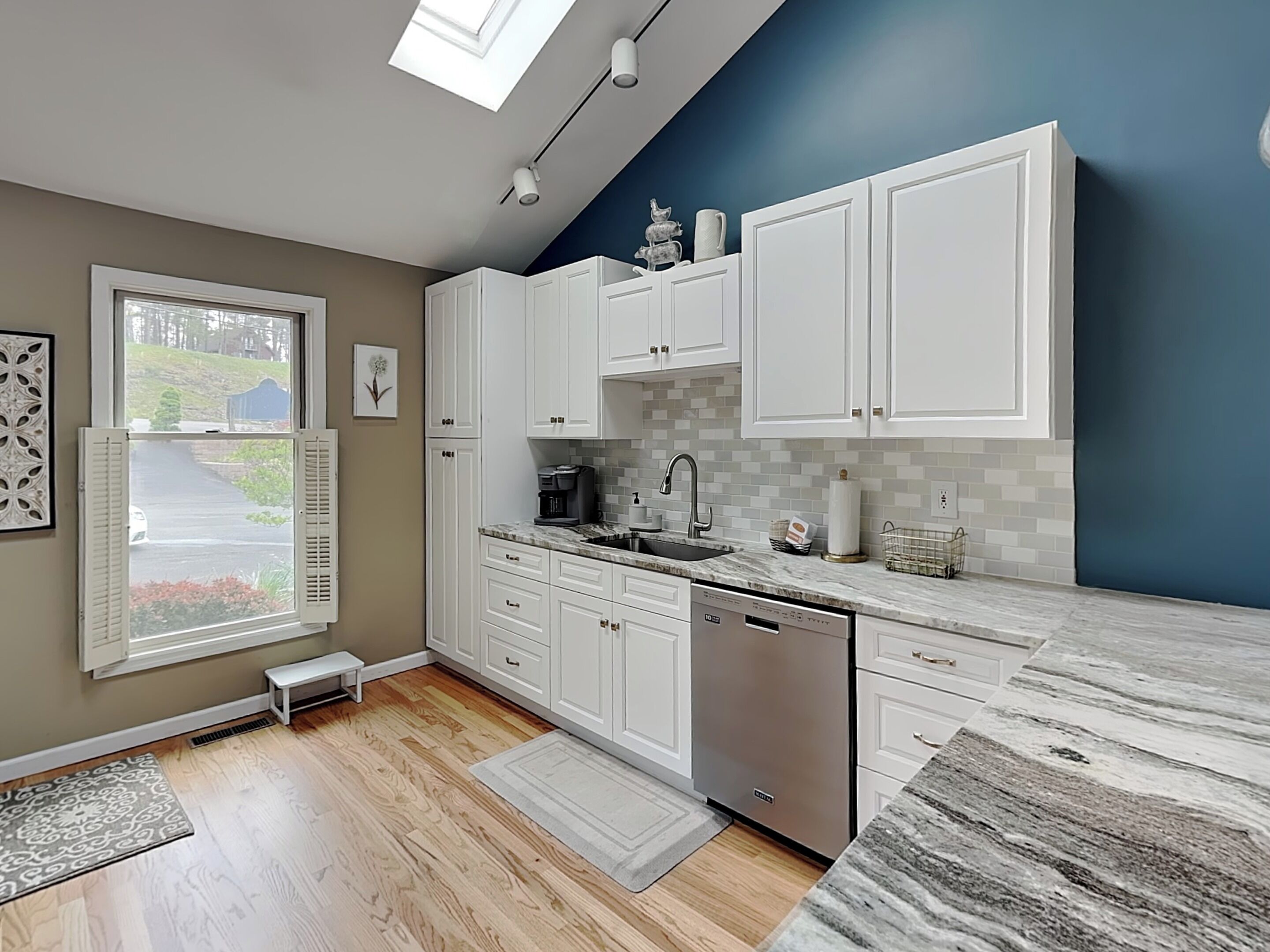 A modern kitchen with white cabinets, a dishwasher, and a window with shutters.