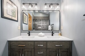 A modern bathroom with a large mirror, two sinks, and a vanity with dark wood cabinetry. - Misty Creek by Taylor Made Deep Creek (McHenry)
