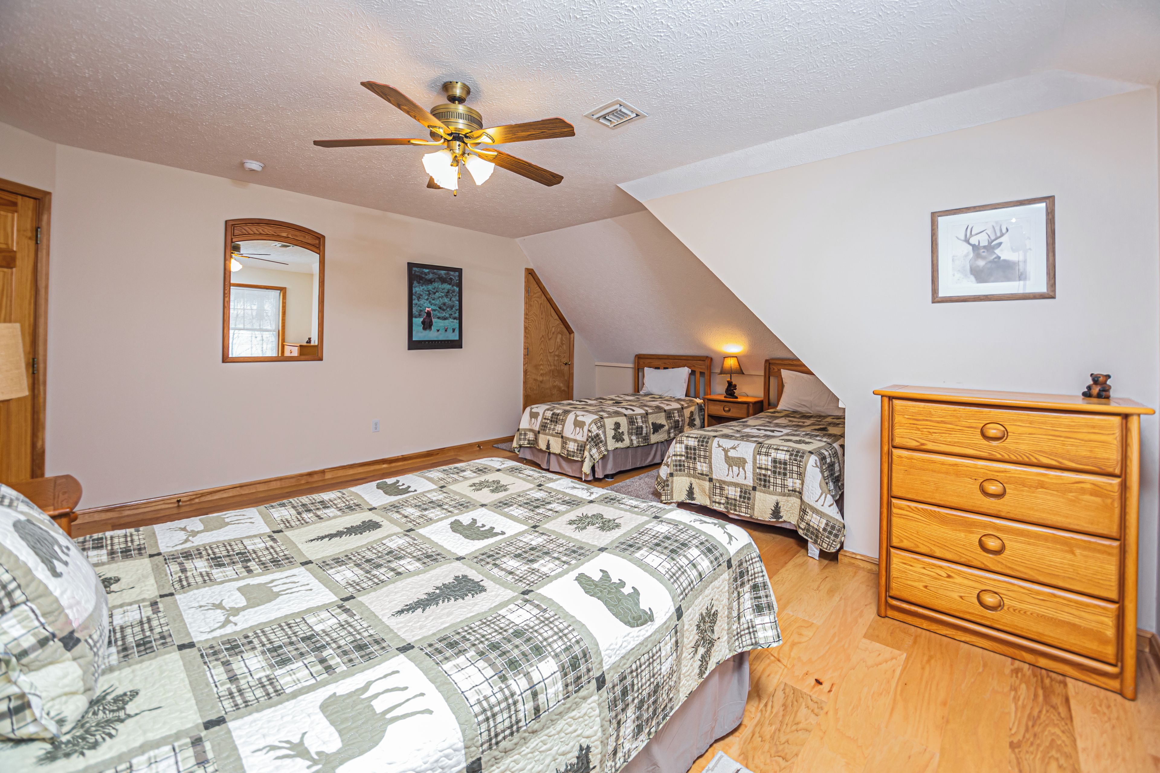 A bedroom with two beds, a ceiling fan, a dresser, and a framed deer picture.