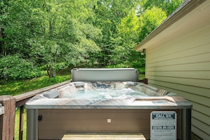 A hot tub in a backyard with a wooden deck and a sign indicating emergency contact information.