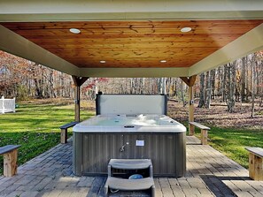 A hot tub under a wooden pergola with a brick patio, surrounded by a wooded area. - Moonrise Retreat by Taylor Made Deep Creek (Swanton)