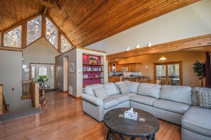 A spacious living area with a large sectional sofa, a round coffee table, and a wooden ceiling with skylights. - Moonrise Retreat by Taylor Made Deep Creek (Swanton)