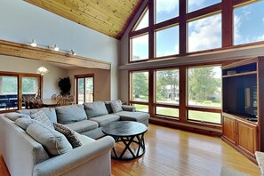 A spacious living room with a large sectional sofa, a round coffee table, and a television. - Moonrise Retreat by Taylor Made Deep Creek (Swanton)
