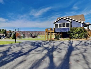 Uma casa residencial com uma quadra de basquete em primeiro plano e uma vista desobstruída de uma paisagem montanhosa ao fundo.