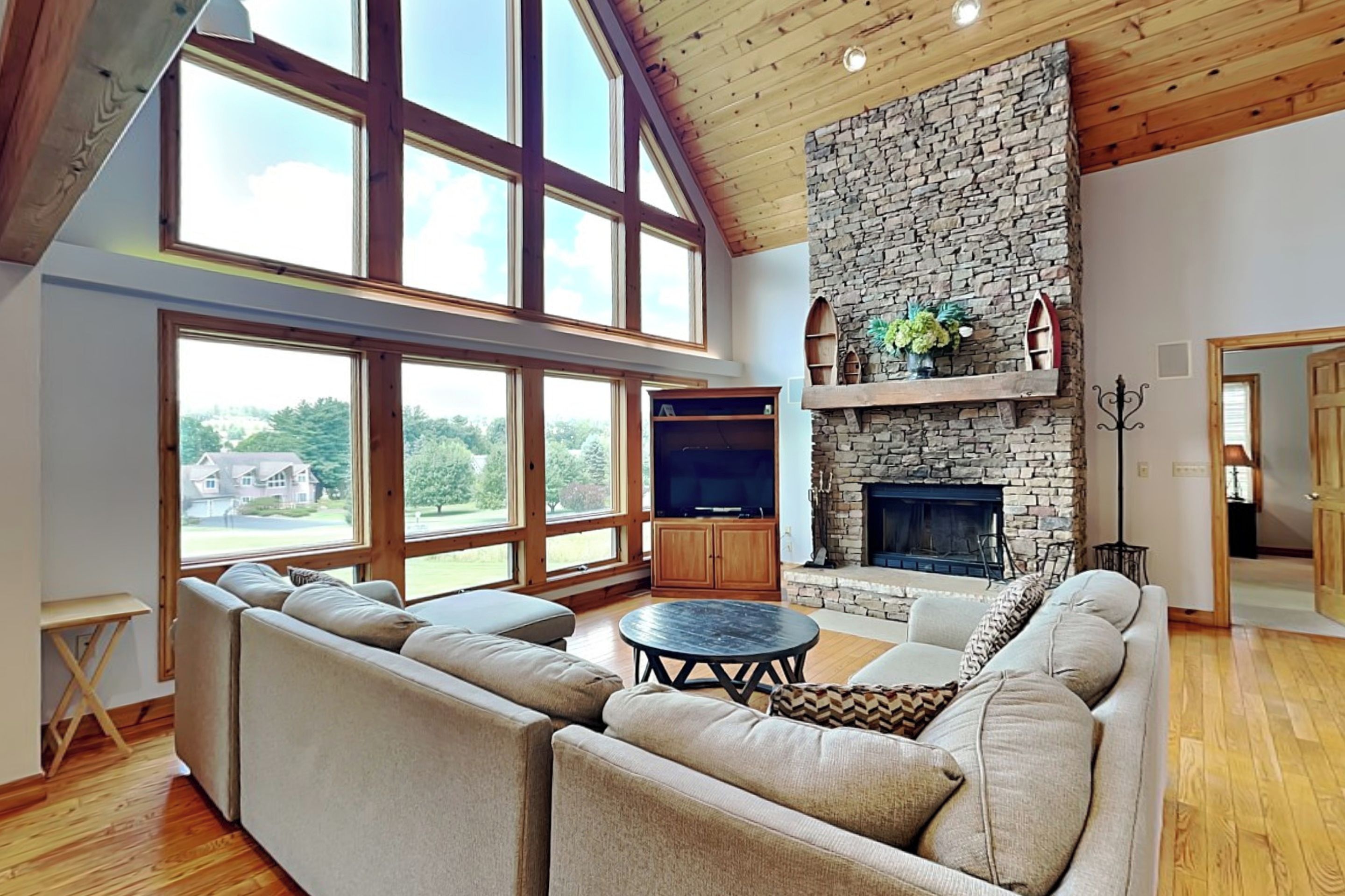 A spacious living room with a stone fireplace, large windows, and a high ceiling.