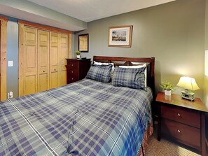 Un dormitorio con cama, armario de madera, mesita de noche con lámpara y un cuadro en la pared.
