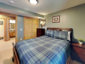 Un dormitorio con cama, armario de madera, mesita de noche, lámpara y un cuadro en la pared.